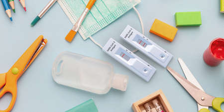 School protection concept. Rapid test, supplies, medical protective mask and sanitizer gel on blue...