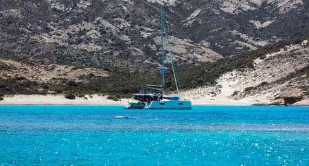 Polyaigos volcanic white sandy beach luxury yacht moored in calm turquoise Aegean sparkle sea blue...