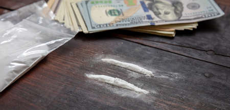 Drugs narcotics addiction concept. Cocaine plastic packets and US dollars banknotes on a table. White powder lines and money closeup.の写真素材