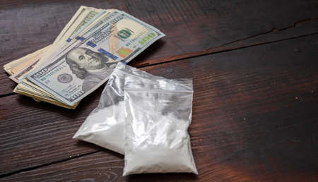 Drugs narcotics business concept. Cocaine plastic packets and US dollars banknotes on a table. White powder addiction and money, copy space, templateの写真素材