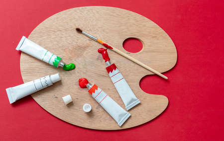 Painting concept. Paintbrushes, colorful paints and wooden artist palette on red color background, Education, Back to School, kids creativity concept.の写真素材