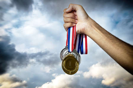 Medals in the athlete hand against a dramatic sky. Winner award, gold silver and bronze. Sport champion victory and success conceptの写真素材