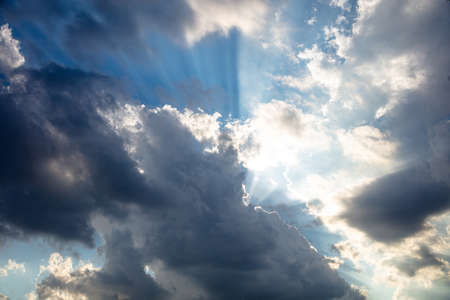 Heavy dark clouds on blue sky background, Sunbeams through the clouds. Fluffy cumulus clouds, cloudscape white and grey colorの写真素材
