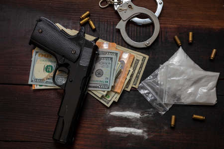 Illegal substances business and arrest. Handcuffs, pistol money and cocaine packets on wooden table background. Drugs smuggling and trafficking conceptの写真素材
