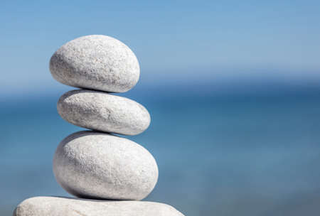 Balance, zen stones, smooth pebbles pyramid stacked on blur blue sea and sky background, sunny day. Feng shui, harmony and peace concept. Copy space, template.の写真素材