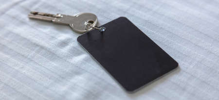 Door key with blank label. Steel key ring, room key and empty black tag for text or number close up view. House, hotel or motel room open, unlock concept. Copy space, templateの写真素材