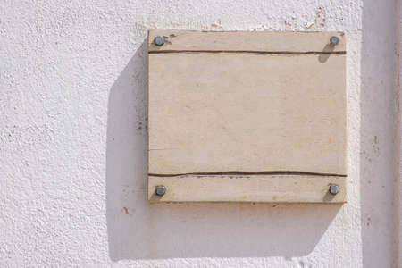 Sign plate mounted with screws on white wall. Blank label mockup, Wooden beige color empty board, business signage template, copy space.の写真素材