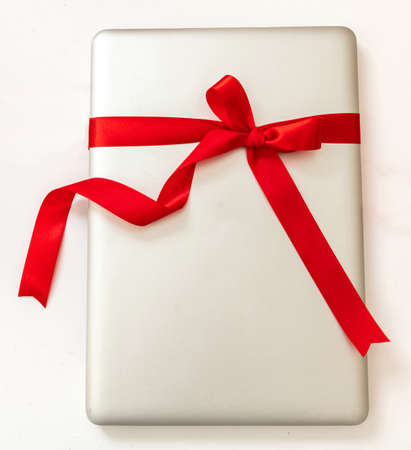 Laptop computer with red ribbon bow, Digital device Christmas gift isolated on white background. Valentine, holiday present, top view.の写真素材