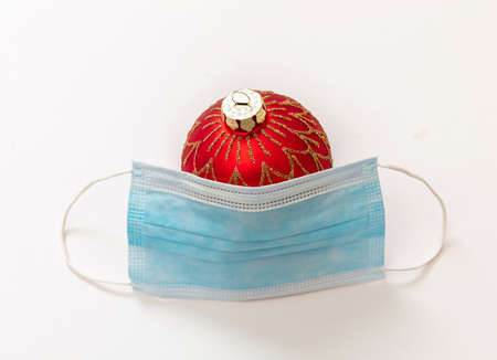 Safe Christmas and New Year holidays in COVID 19 days. Xmas ball bauble and Corona virus protective mask isolated on white background. Traditional winter season events and celebration during pandemicの写真素材