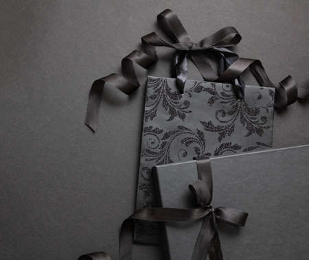 Black Friday concept. Black shopping bag and gift box with ribbon bow on black background, top view, Luxury purchase, holiday giftの写真素材