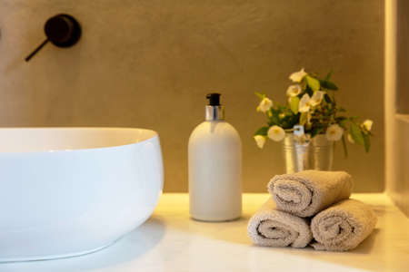 Bathroom towels roll ups, soap dispenser and white sink basin on a table. Modern bathroom interior detail.の写真素材