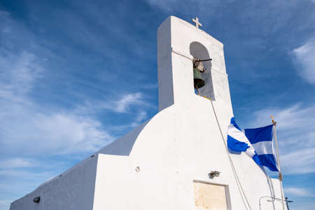 Serifos island, Greece. Small old chapel, white walls and bell tower, Greek flag waving on church...