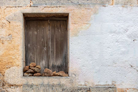 Abandoned  home concept. Aged window with wooden planks shutters kept closed with pile of stones on...