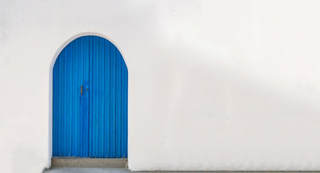 Blue wooden vintage closed door with arch on an empty whitewashed wall background. Cyclades Greek island architecture, blank copy space card template advertise.の写真素材