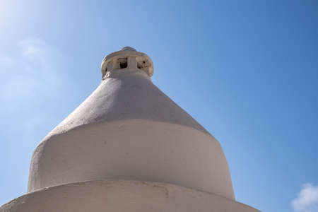 Round whitewashed chimney on top of building roof, Greek island, Greece. Circle smokestack exterior construction on a house rooftop. Blue sky background.の写真素材