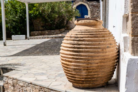 Handmade old ceramic amphora with cover in a garden, traditional clay craft container. Greek island house exterior decoration, Chora village Greece.の写真素材