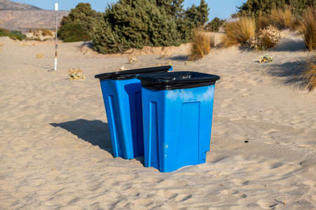 Keep The Beach Clean environmental awareness concept. Blue big rubbish bins in the middle of sandy coast. Garbage cans dumpsters trashcans on soft sand at seaside. Summer sunny day nature background.の写真素材