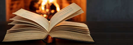 Reading and relax near the fire, Book open, fireplace burning firewood background. Christmas holiday cozy warm home interior.の写真素材