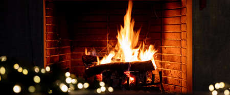 Fireplace, Christmas lights decoration and burning wood logs. Bonfire fire flames. Cozy living room interior, winter holidays relaxation and warm festive homeの写真素材