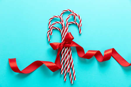 Candy canes bunch on blue background. Christmas peppermint red white candies with red ribbon bow. Merry Xmas greeting card templateの写真素材