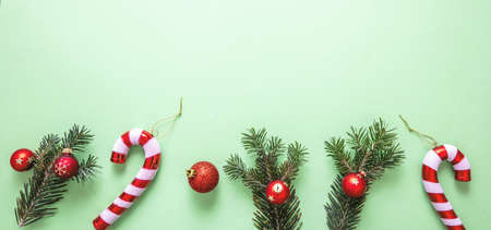 Christmas decoration border on pastel green background. Fresh fir twig, red baubles and candy canes banner. Merry Xmas New Year greeting cardの写真素材