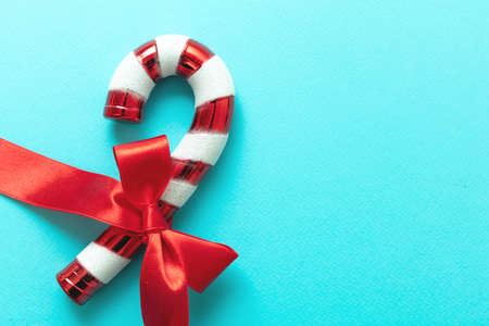 Candy cane with red ribbon bow isolated on blue background. Christmas peppermint red white dessert. Merry Xmas greeting card template, copy spaceの写真素材