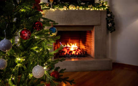 Christmas warm cozy living room background. Xmas tree decoration, burning fireplace, garlands baubles and lights, winter holiday home.の写真素材