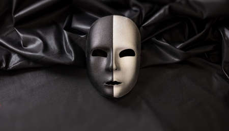 Carnival Venetian two faced mask, half black half silver on wavy dark satin textile background. Traditional festival disguise, Mardi Gras event masqueradeの写真素材