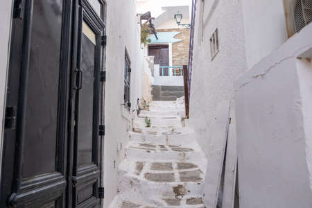 Cyclades, Greece. Ios, Nios island, Chora. Whitewashed buildings and narrow cobblestone alley, traditional architecture. Closed doors, empty paved street.の写真素材