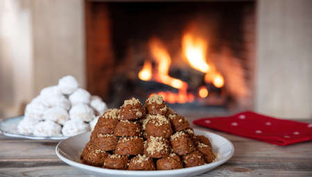 Christmas Greek desserts. Traditional homemade melomakarona and kourabiedes on a table, burning fireplace backgroundの写真素材