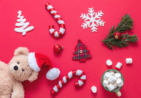 Christmas decoration flat lay on red color background. Xmas baubles teddy bear with Santa hat and candy canesの写真素材