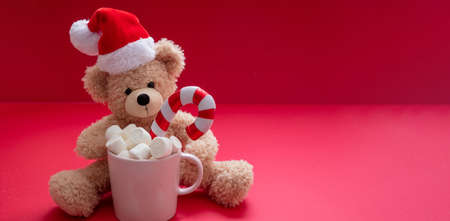 Christmas hot beverage and Santa teddy, chocolate mug with marshmallows and candy cane on red color background, space.の写真素材