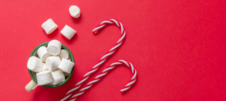 Christmas hot beverage, chocolate mug with marshmallows and candy canes on red color background,...