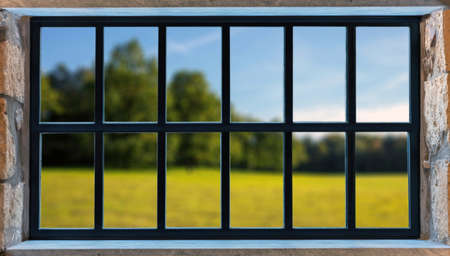 Metal frame window on a stone wall. Black color aluminum grid, blur nature background outdoors. House in countryside, window with viewの写真素材