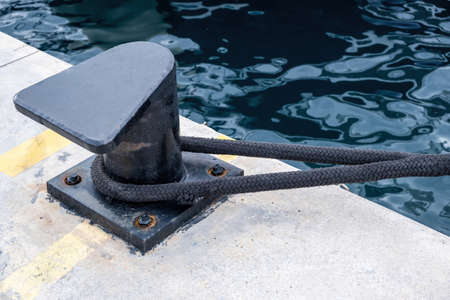 Ship mooring rope around a port bollard on harbor pier, rippled sea water background, copy space....