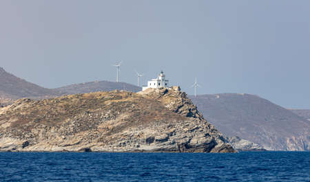 Korakas lighthouse on rocky cliff at Naoussa village Paros island Cyclades Greece. White stonewall beacon at cape, calm Aegean sea. Wind generators and blue sky backgroundの写真素材