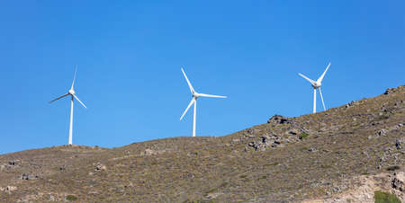 Renewable power energy, Wind turbine, electric generator on a rocky hill, clear blue sky background,...