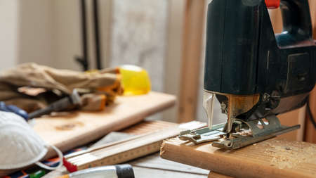 Electric jigsaw cutting wood. Construction industry, carpenter workshop, work bench table closeup viewの写真素材