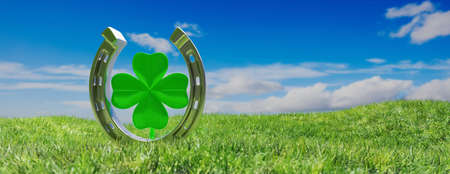 Silver shiny horseshoe with green four leaf clover on grass field blue cloudy sky background. Lucky...