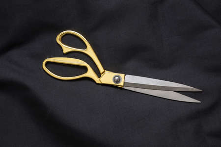 Open scissors with gold handle on black color cloth background. Tailor, fashion and Black Friday sale conceptの写真素材