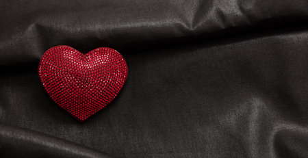 Valentine day, love celebration. Red color ruby heart jewel on empty black luxury silk, satin...