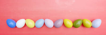 Pastel color Easter egg in a row on red wood, header. Spring Holiday celebration, top view, copy space. 3d renderの写真素材