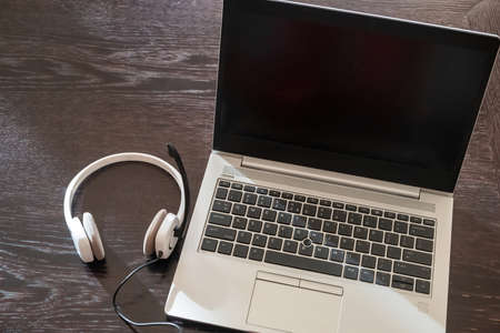 Headset on a laptop, blank screen, wooden table background, Call center, home office, customer support, help desk, copy space, template.の写真素材