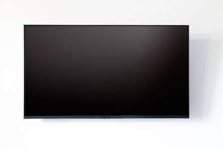 TV blank LED screen on white wall background. Black empty television display front view, copy space,...