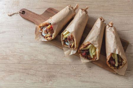Shawarma Gyro pita on wooden table. Greek food, sliced meat, potato, tomato and tzatziki, paper wrap, close up view.の写真素材