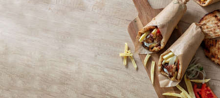 Gyro pita Shawarma preparation on wooden table, top view. Greek food, sliced meat, potato, tomato and tzatziki, paper wrap. Banner, Copy spaceの写真素材