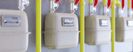 Natural gas meter in a row. Yellow plumbing pipe on residential building wall. Household energy...