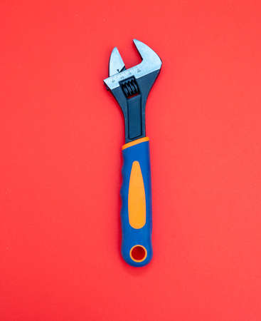Adjustable wrench with graduated scale, orange, blue color rubber handle on red background. Hand tool, new metalwork implement for mechanical, locksmith, plumber.の写真素材