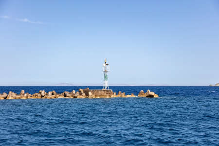 Beacon on cement construction at breakwater concrete block at Ermoupolis city port, Syros island, Cyclades Greece. Aegean ripple sea, blue skyの写真素材
