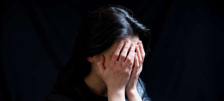 Young woman covering eyes, sad and frightened in a dark room, copy space. Fear and despair concept